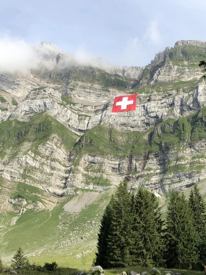 Schweizer Alpen mit wehender Landesflagge vor blauem Himmel – ideal für eSIM-Reisende in der Schweiz
