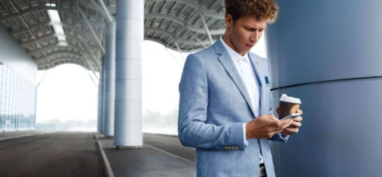 redhaired businessman drinking coffee using phone at airportmin 1 540x250